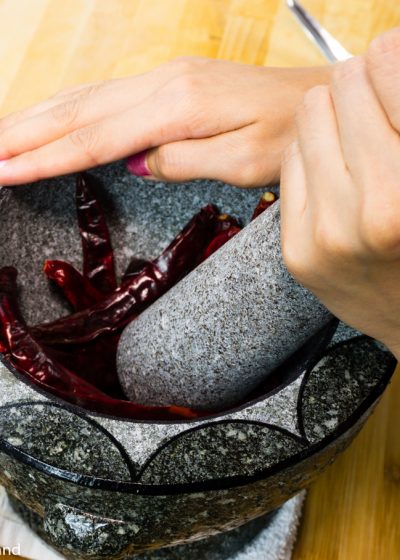 Whole Thai chilies being prepared in a mortar with a pestal