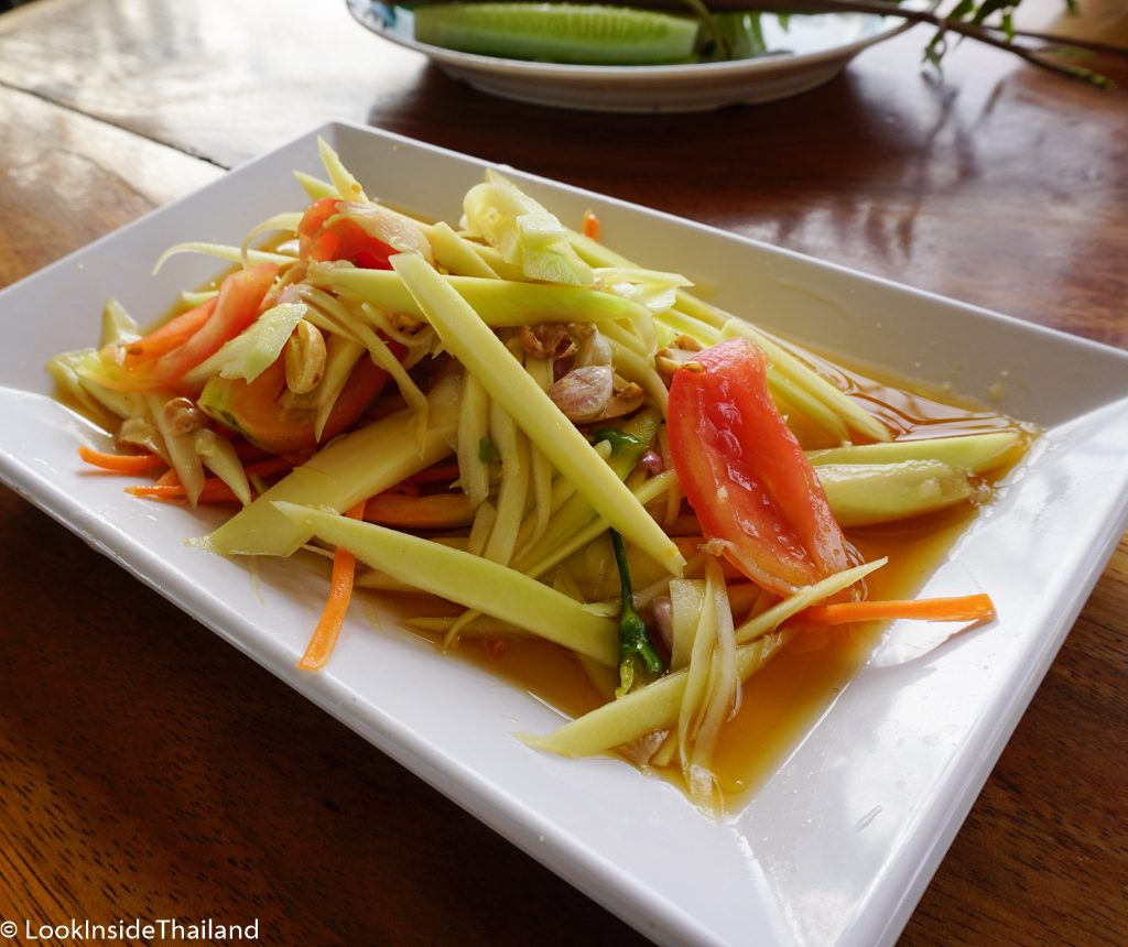 Som tam mango on a white plate tomatoes garlic peppers